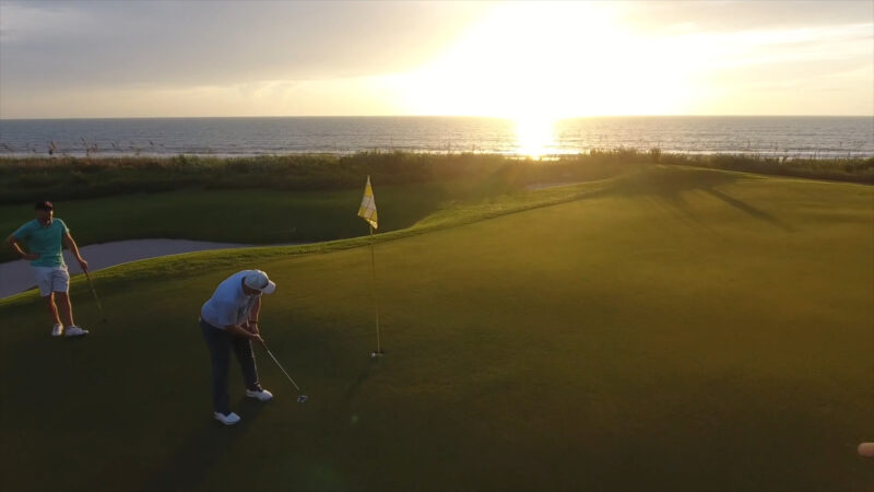 Two golfers putting on a green beside the ocean at sunset in Florida
