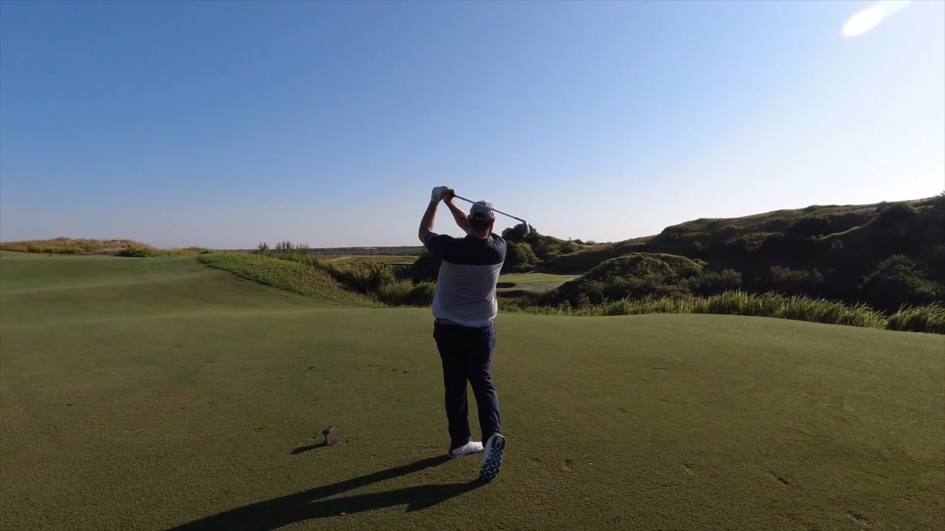 A golfer completes a drive on a Florida golf course with rolling terrain and blue sky