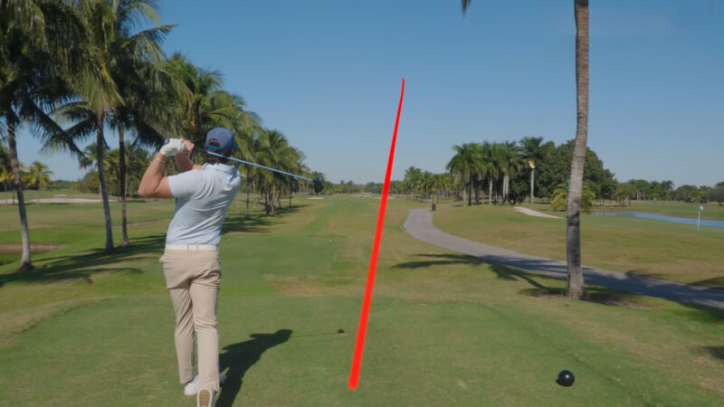 Golfer follows through on a powerful drive, with a red line tracing the golf ball’s flight path