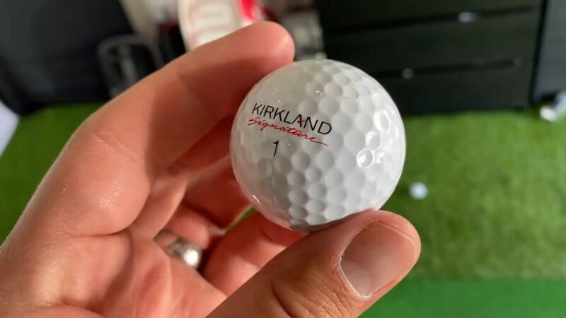 Close-up of a hand holding a Kirkland Signature golf ball indoors