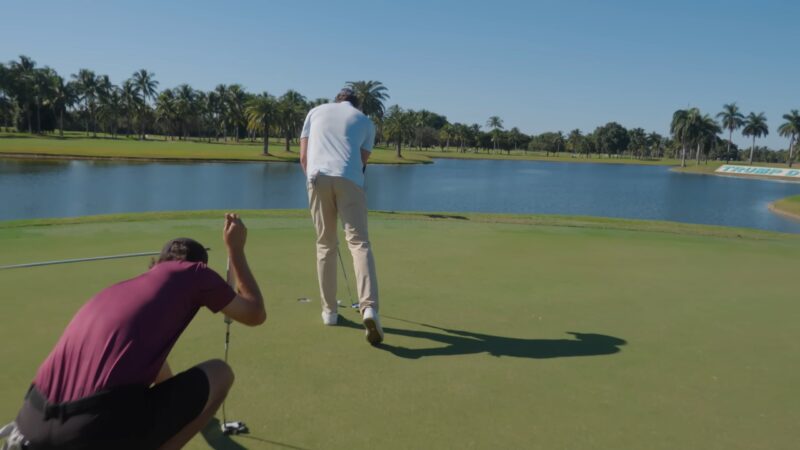 Two golfers putting on a green beside a lake at a sunny Florida golf course