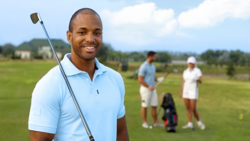A smiling golfer holds a club on the course, with other players chatting in the background during a charity golf tournament